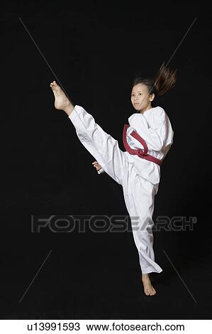 Stock Image - Young woman performing round kick. Fotosearch