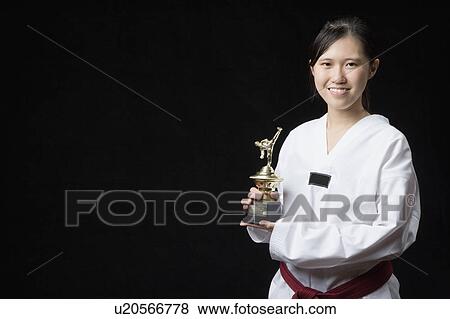 Stock Photo - Portrait of a young woman holding a trophy and smiling. Fotosearch