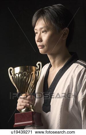 Stock Image - Close-up of a young man holding a trophy. Fotosearch