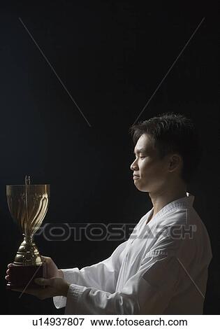 Side profile of a young man holding a trophy View Large Photo Image Stock Photo - Side profile of a young man holding a trophy. Fotosearch