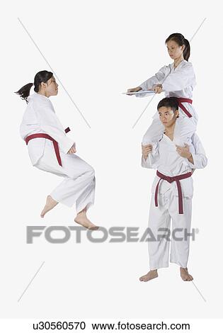 Stock Image - Side profile of a young man practicing kickboxing with two young women. Fotosearch