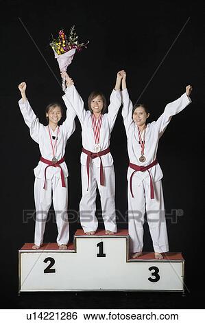 Stock Photograph - Three young women raising their hands on a winners podium. Fotosearch