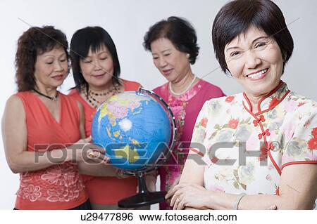 Stock Photograph - Portrait of a mature woman smiling with her friends looking at a globe. Fotosearch
