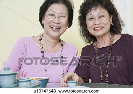 Stock Photo - Portrait of two senior women sitting at a table and smiling. Fotosearch