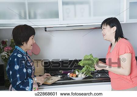 Side profile of a senior woman and her daughter preparing food in a kitchen View Large Photo Image Stock Image - Side profile of a senior woman and her daughter preparing food in a kitchen. Fotosearch