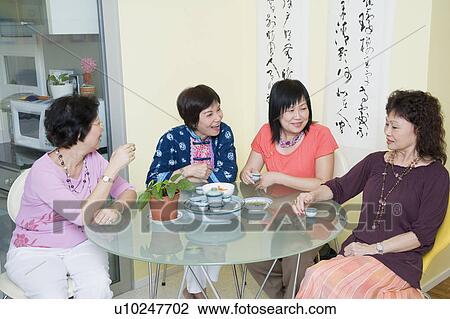 Stock Image - Three senior women and a mature woman sitting at a table. Fotosearch