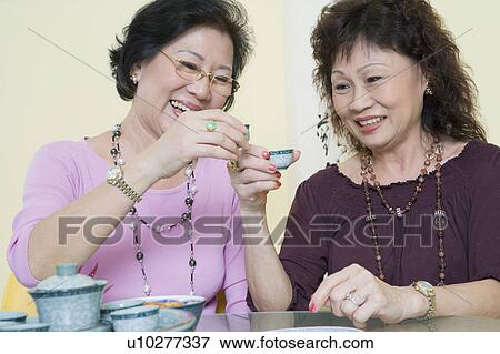 Two senior women sitting at a table and toasting with tea cups View Large Photo Image Stock Photo - Two senior women sitting at a table and toasting with tea cups. Fotosearch