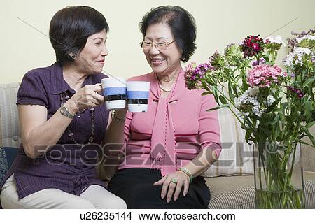 Picture - Close-up of two senior women toasting with cups and smiling. Fotosearch