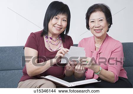 Portrait of a mature woman and a senior woman holding photographs and smiling View Large Photo Image Picture - Portrait of a mature woman and a senior woman holding photographs and smiling. Fotosearch