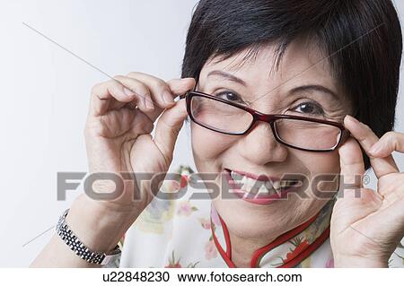 Stock Image - Portrait of a senior woman adjusting her eyeglasses and smiling. Fotosearch