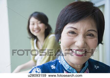 Stock Photo - Portrait of a senior woman smiling with her granddaughter standing behind her. Fotosearch