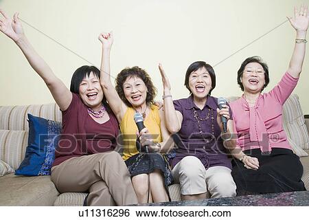 Stock Photograph - Three senior women and a mature woman singing in front of microphones with their hands raised. Fotosearch