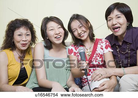 Picture - Two young women singing with their grandmothers into microphones. Fotosearch