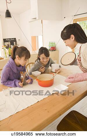 Stock Photography - Three young women chatting at dinning table. Fotosearch