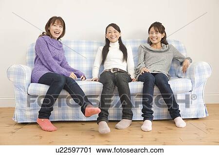 Stock Image - Three young women sitting on sofa. Fotosearch