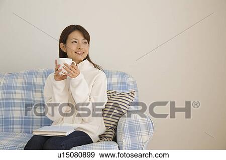 Stock Photo - Young woman holding cup on sofa. Fotosearch