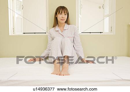 Stock Photo - Young woman sitting on bed. Fotosearch