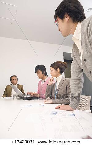 Stock Image - Four people discussing in meeting room. Fotosearch