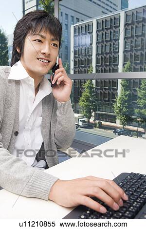 Stock Photography - Young man talking over mobile phone in office. Fotosearch