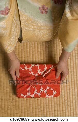 Stock Photo - Young woman in kimono holding out wrapped gift. Fotosearch
