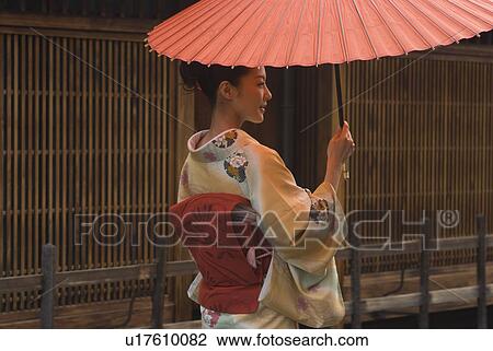 Stock Image - Young woman in kimono holding paper umbrella. Fotosearch