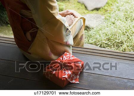 Stock Image - Young woman in kimono sitting at veranda. Fotosearch