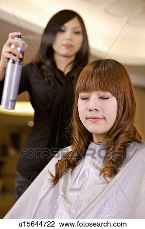 Stock Image - Hairdresser using hairspray on customer's hair, Hair Salon. Fotosearch