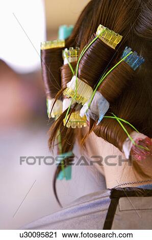 Stock Image - Young woman having curling her hair with curlers, Hair Salon. Fotosearch