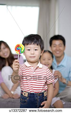 Stock Photo - Family, a boy showing his lollipop, family in background. Fotosearch