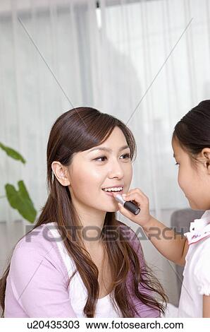Stock Image - Family, daughter applying lipstick to mother. Fotosearch