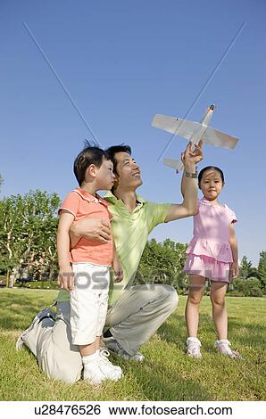 Stock Photograph - Family, father and two children playing toy airplane in a park. Fotosearch