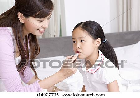 Stock Photography - Family, mother applying lipstick to daughter. Fotosearch
