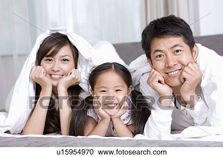 Stock Image - Family, Portrait of family lying in bed together, playful. Fotosearch