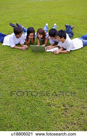 Stock Image - Five teenagers lying on the lawn and looking at the laptop together, Teenager. Fotosearch