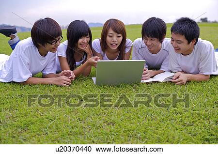 Stock Image - Five teenagers lying on the lawn and using laptop, Teenager. Fotosearch
