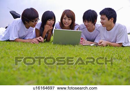 Stock Photo - Five teenagers lying on the lawn and looking at the laptop together, Teenager. Fotosearch