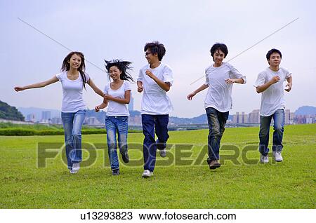 Stock Image - Five teenagers running on the lawn with arms outstretched, Teenager. Fotosearch