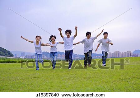 Stock Image - Five teenagers running on the lawn with arms outstretched, Teenager. Fotosearch