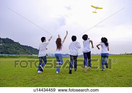 Stock Photo - Teenagers running on the lawn and looking up together, chasing a model airplane. Fotosearch