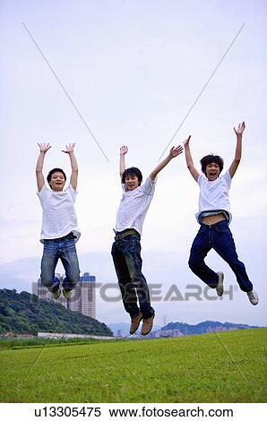 Stock Photography - Three boys jumping on the lawn with arms outstretched, Teenager. Fotosearch