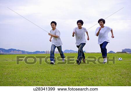 Stock Photo - Three boys running on the lawn together, Teenager. Fotosearch