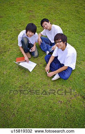 Stock Image - Three boys sitting on the lawn and looking up, Teenager. Fotosearch