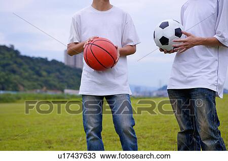Stock Image - Two boys holding basketball and football and standing on the lawn, Teenager. Fotosearch