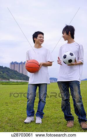Stock Image - Two boys holding basketball and football and looking at each other, Teenager. Fotosearch