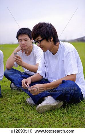 Stock Image - Two boys sitting on the lawn and listening music, Teenager. Fotosearch