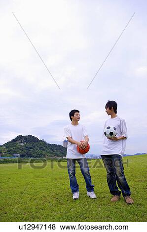 Stock Photo - Two boys standing on the lawn and holding basketball and football, Teenager. Fotosearch