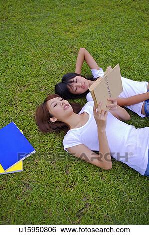 Stock Photograph - Two girls lying on the lawn and reading a book, Teenager. Fotosearch