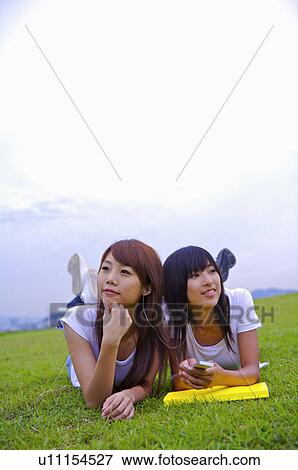 Stock Photo - Two girls lying on the lawn, listening music and looking away, Teenager. Fotosearch