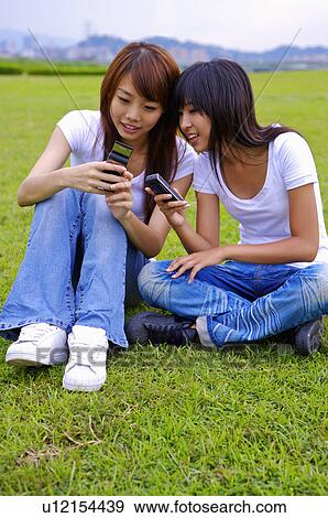 Two girls sitting on the lawn and holding mobile phone, Teenager View Large Photo Image Stock Photo - Two girls sitting on the lawn and holding mobile phone, Teenager. Fotosearch