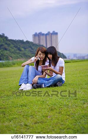 Stock Photo - Two girls sitting on the lawn together, Teenager. Fotosearch